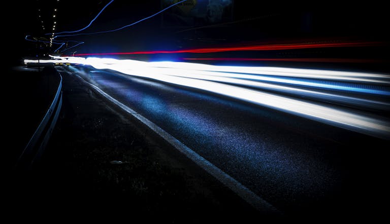 Long exposure shot of vibrant light trails on a highway at night, showing urban motion and speed.